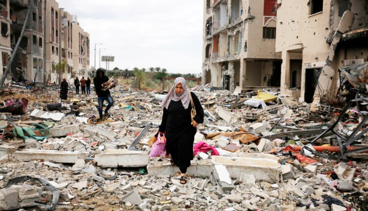 Warga Jalur Gaza berjalan diantara reruntuhan gedung.
